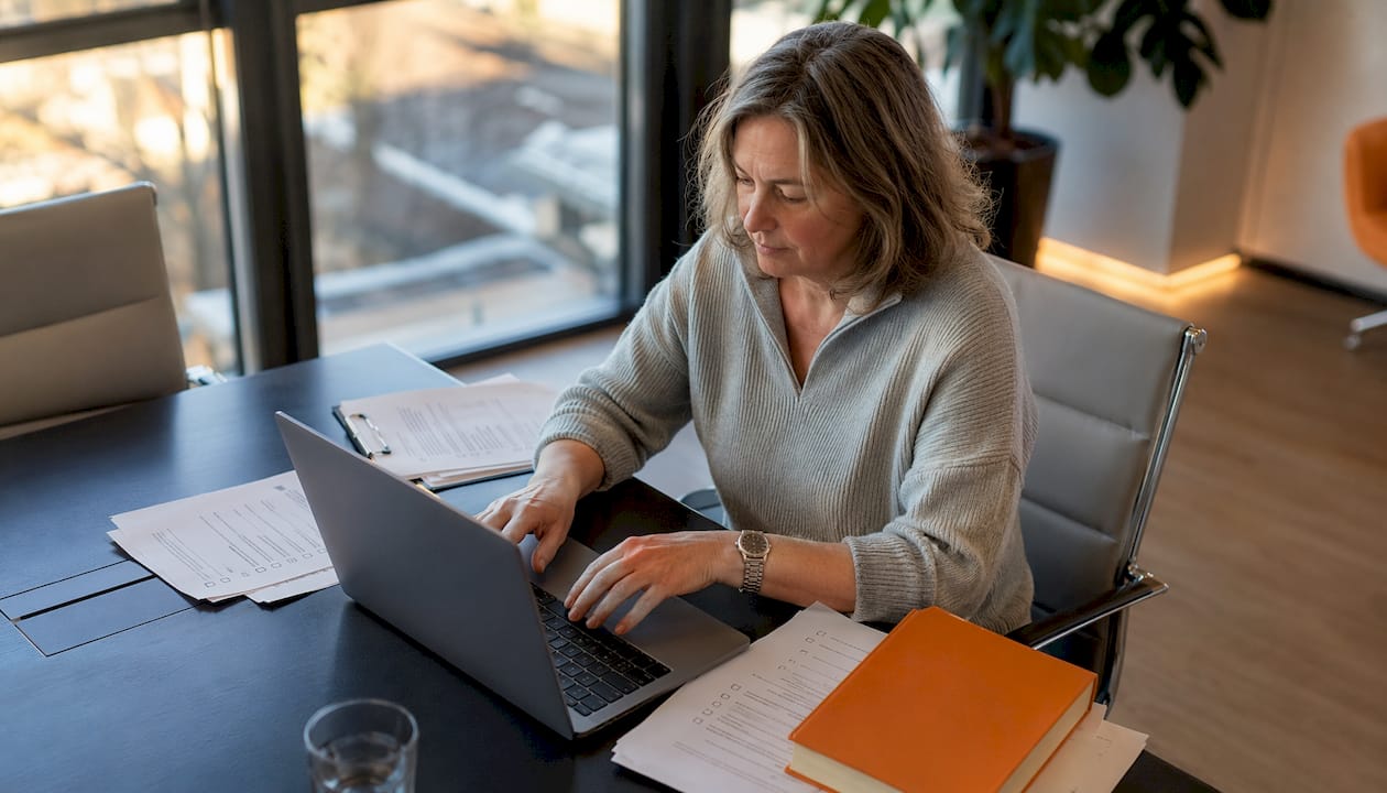 Hände tippen auf der Tastatur, während neben dem Computer DSGVO-Dokumente liegen.
