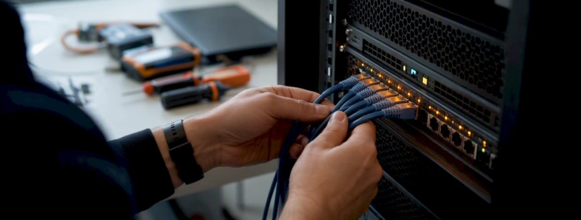 Hände schließen Kabel an einem Serverschrank an.