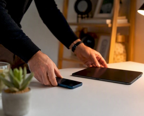 Ein Paar Hände legt Smartphone und Tablet ordentlich auf den Schreibtisch.