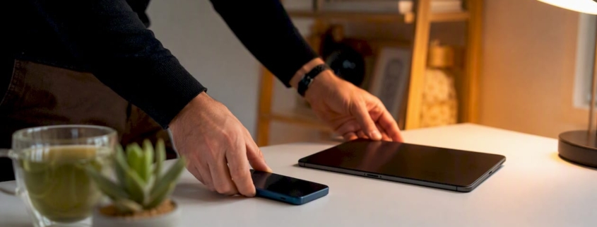 Ein Paar Hände legt Smartphone und Tablet ordentlich auf den Schreibtisch.